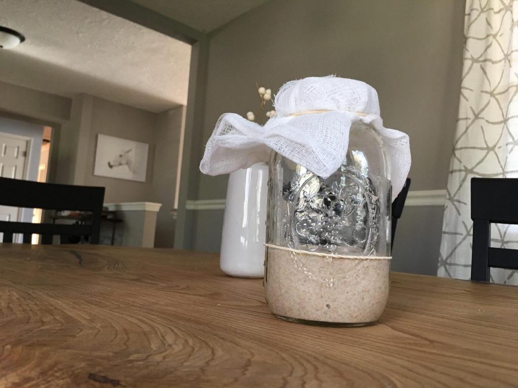 A mason jar containing a sourdough starter after the fifth day of it's feeding. There's a rubber band wrapped around the jar to mark the level of the starter and a cheese cloth covering the mouth of the jar